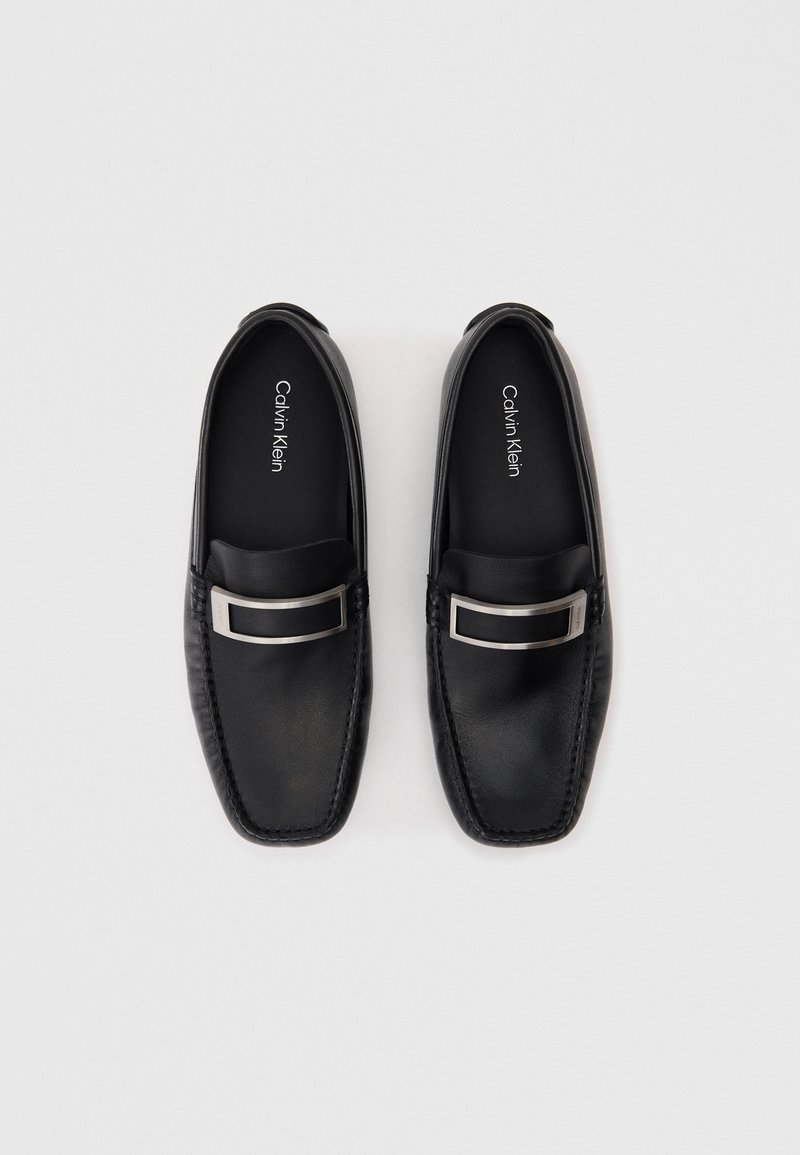 Schwarze Lederloafers mit einem quadratischen silbernen Schnallenakzent. Runde Zehenform und gestickte Details entlang der Kanten. Markenname innen sichtbar.