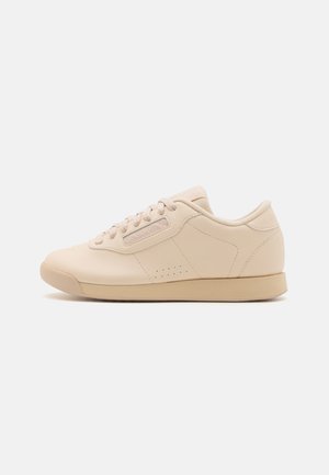 Beige leather sneakers with a rounded toe, flat rubber sole, six eyelets, and subtle perforations along the sides. Simple, streamlined design.