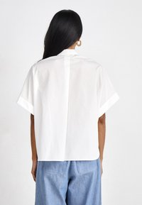 White short-sleeve shirt with a relaxed fit and simple design. Features a classic collar and a straight back hem. Made of lightweight fabric.