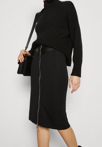 Černá tužková sukně s elegantním designem, která má přední zip, doplněná černým svetrem s žebrováním. Hladká textura a přiléhavý střih.