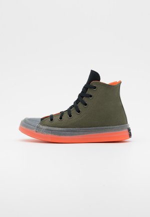 Høj-top sneaker i olivengrønt lærred med sorte snørebånd, sort tung, gennemsigtig tåhætter og levende orange sål og indvendig foring.