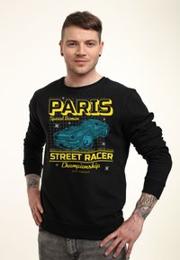 Felpa nera con stampa grafica che presenta la scritta "PARIS" e un design di auto in blu e giallo. Maniche lunghe e polsini a costine. Vestibilità casual.