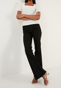 Biała bluzka z kwadratowym dekoltem i bufiastymi rękawami, w połączeniu z czarnymi spodniami w kant i przejrzystymi butami na obcasie. Gładkie tekstury i dopasowana sylwetka.