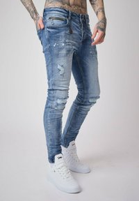 Skinny-fit jeans in light blue denim with distressed details, frayed hems, and subtle fading. Worn with white sneakers.