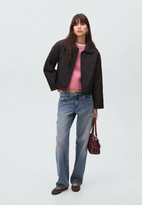 Jachetă neagră umplută, pulover roz tricotat, blugi lejeri albăstrui, pantofi maro închis cu tălpi plate și cu ținte, și o geantă mică maro bordeux.