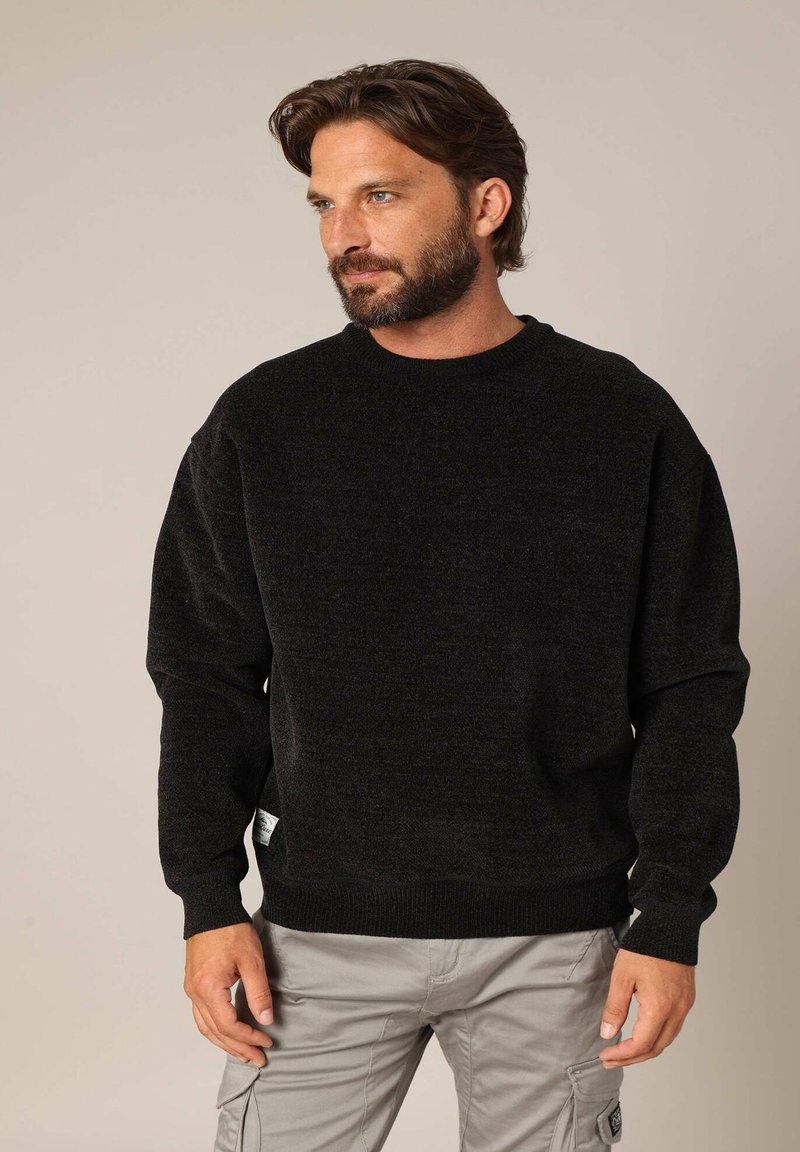 Pull en maille noir avec un col rond et des épaules tombantes. Présente une finition texturée et des poignets et un ourlet côtelés pour plus de détails.