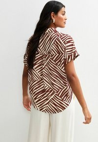 Camisa de manga corta con un patrón a rayas en tonos marrón y crema, con un corte relajado y dobladillo curvado, fabricada en un tejido ligero.