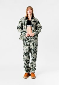 Conjunto que incluye una chaqueta holgada de estampado verde y beige y pantalones a juego, combinados con un top corto negro y botas marrones.