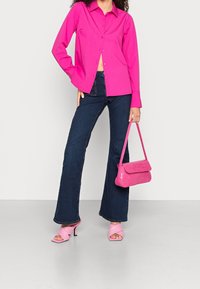 Fuchsia skjorta med knappar, mörkblå utsvängda jeans, rosa klacksandaler och en liten rosa texturerad handväska.