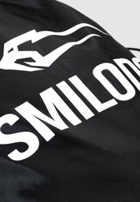 Tela negra con un logo y texto blanco prominentes. La textura parece ligeramente elevada con un patrón de cuadrícula, lo que enfatiza la durabilidad.