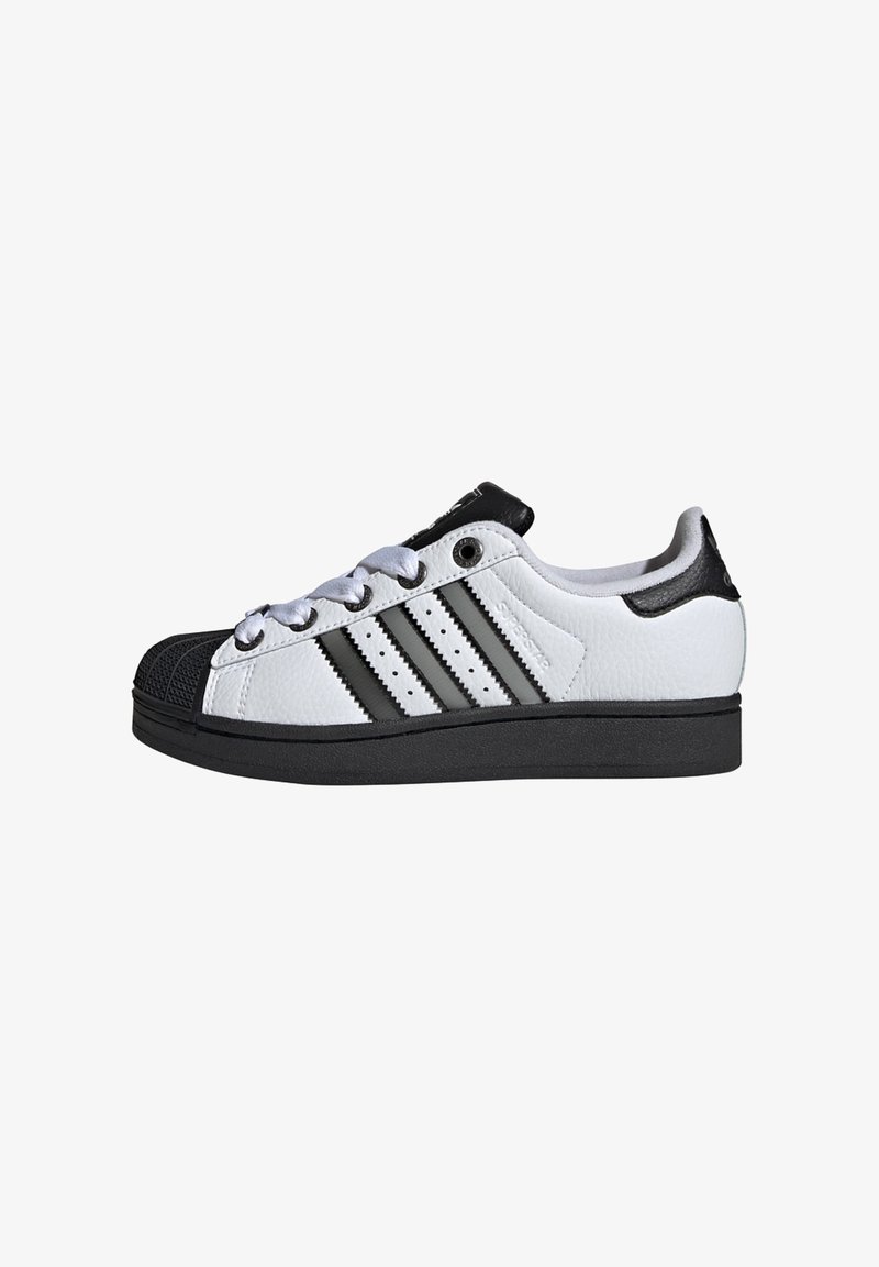 Biele kožené tenisky s čiernym gumovým špičkovým krytom a čiernymi akcentmi. Obsahujú tri čierne pruhy, okrúhle šnúrky a textúrovanú podrážku.