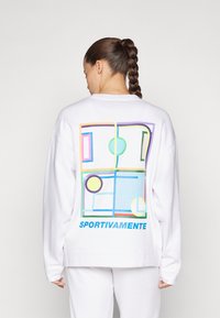 Fehér pulóver, hátul színes geometriai mintával, amely téglalapokból és körökből áll, valamint a "SPORTIVAMENTE" felirattal kék színben.