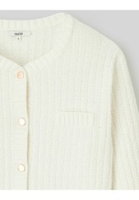 Cardigan blanc en tricot avec une texture côtelée, col rond et une seule poche poitrine. Présente des boutons en or rose sur le devant.