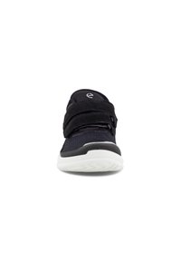 Baskets noires de sport avec tige en mesh, deux sangles Velcro et semelle blanche. Présentent une surface texturée et un talon courbé.