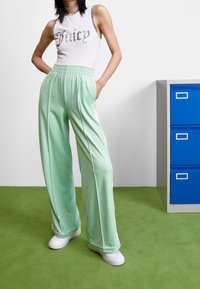 Světle mátové tepláky s volným střihem a elastickým páskem, spojené s bílým tílkem s nápisem "Juicy" ve tmavém písmu.