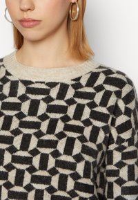 Maglione lavorato a maglia in beige e nero con un motivo geometrico di forme interconnesse, scollatura rotonda e tessuto morbido e textured.