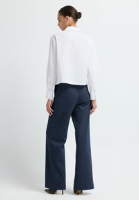 Blusa bianca corta con maniche lunghe, abbinata a pantaloni larghi a righe blu navy e tacchi a spillo neri. Design semplice, tessuto morbido.