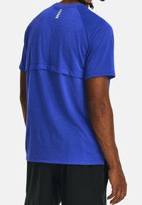 Modré atletické tričko s texturovaným vzorem, krátkými rukávy a horizontálním švem. Na zadní straně je výrazný reflexní prvek.