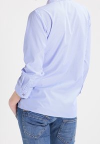 Jasnoniebieska i biała koszula w pionowe paski z długimi rękawami, z zapięciem na guziki i klasycznym kołnierzykiem, zestawiona z dżinsami.