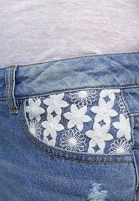 Jeansshorts med en vit blommig broderidesign på höger bakficka, i en ljusblå tvätt med slitna detaljer.
