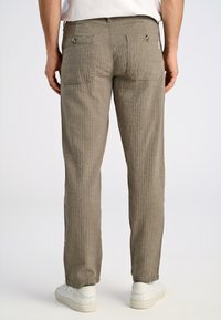 Beige gestreepte broek met een rechte pasvorm, twee achterzakken met metalen knopen en een textuurstof. Gepaard met witte sneakers.