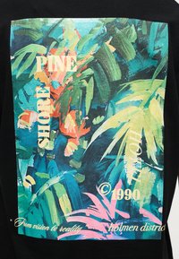 Αφαιρετικά τροπικά φύλλα σε πράσινο, μπλε, ροζ και πορτοκαλί με κείμενο "SHORE PINE," "©1990," και "From vision to reality holmen district" σε μαύρο ύφασμα.