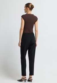 Bruine geribbelde top met korte mouwen en een doorschijnende, gerafelde halslijn, gecombineerd met zwarte tailleursbroek en zwarte haksandalen.