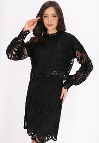 Completo in pizzo nero a due pezzi con un design testurizzato caratterizzato da motivi floreali, maniche a palloncino e scollatura e orlo a scallop.