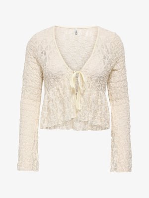 Cardigan corto in pizzo color crema con maniche lunghe, scollo profondo a V e chiusura con laccio sul davanti.