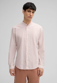 Camicia a maniche lunghe a righe con colletto alla cinese, di un tenue rosa e bianco. Presenta una chiusura con bottoni e un leggero orlo curvo nella parte inferiore.