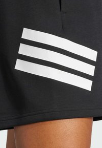Černé sportovní kraťasy s čtyřmi bílými vodorovnými pruhy na straně, vyrobené z měkké, elastické látky s hladkou texturou.
