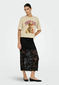 Beige katoenen t-shirt met een teddybeer-afbeelding, gecombineerd met een zwarte kanten midi-jurk met bloemmotieven en een gekartelde zoom.