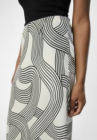 Hvid nederdel med sort abstrakt linjemønster, glat tekstur, høj talje-design, viser sidesøm og del af en hånd, der holder den.