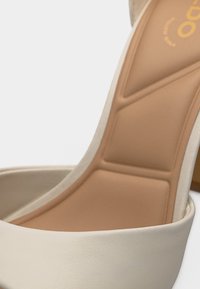 Gros plan de l'intérieur d'une chaussure à talon haut beige avec une semelle intérieure rembourrée et des bords extérieurs lisses.