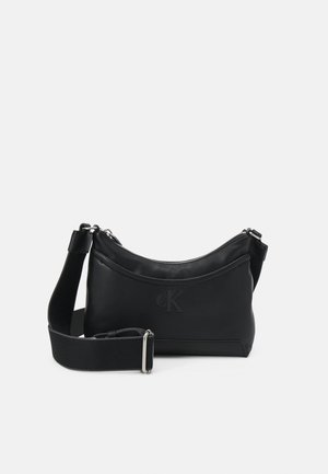 Sac bandoulière en cuir noir avec sangle large réglable, fermeture éclair et logo CK embossé sur l'avant.