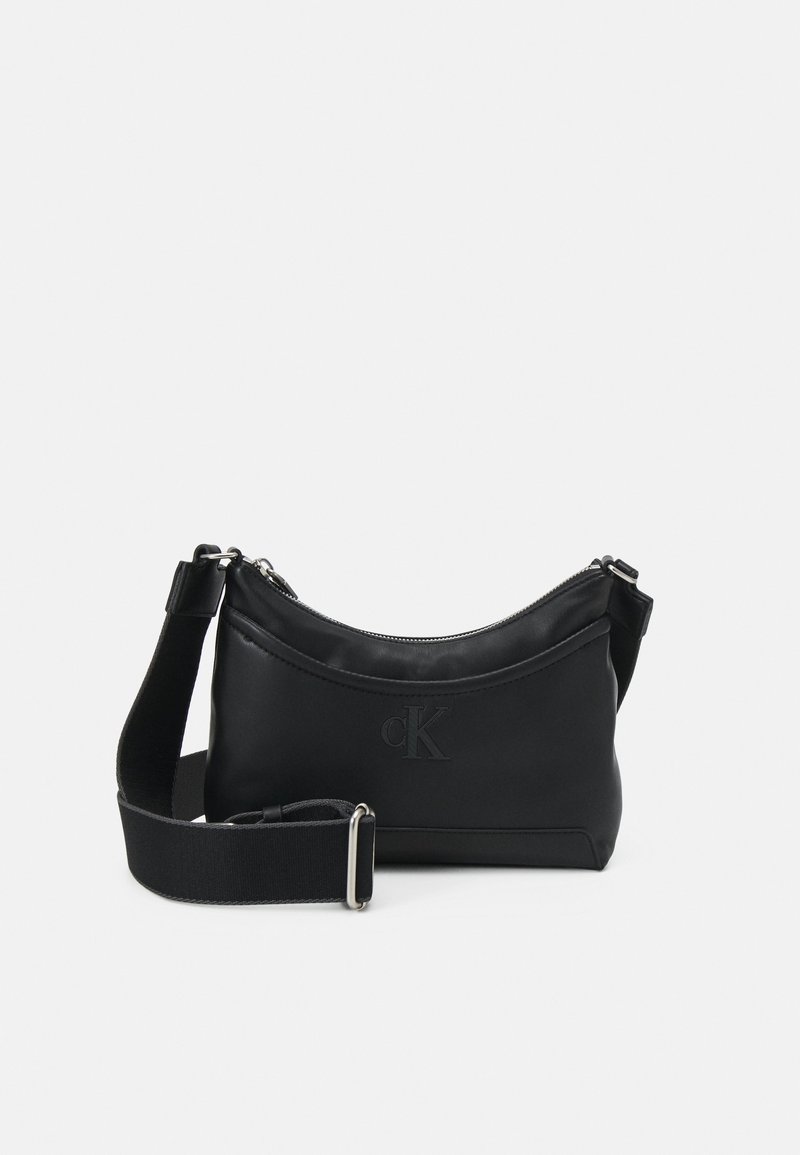 Sac bandoulière en cuir noir avec sangle large réglable, fermeture éclair et logo CK embossé sur l'avant.