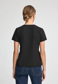 Czarna bawełniana koszulka z krótkim rękawem, okrągłym dekoltem i dopasowanym krojem, noszona z ciemnoniebieskimi dżinsami z wysokim stanem.