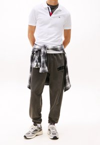 Vit polo skjorta med krage i marinblått och rött, grå sweatpants med Tommy Hilfiger-logotyp, och grå sneakers. En svart-och-vit rutiga skjorta knuten runt midjan.