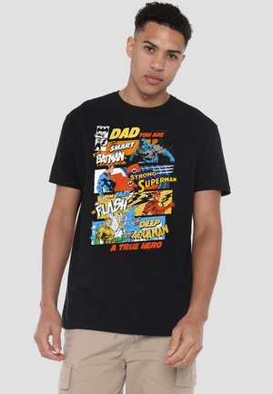Man wearing black T-shirt with colorful comic-style text and images of Batman, Superman, Flash, and Aquaman praising dad as a true hero.