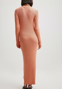 Maxi-jurk met lange mouwen van geribbelde stof in zachte perzikkleur, met een aansluitende pasvorm en een ronde halslijn, met een soepele textuur en zonder zichtbare sluitingen.