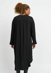 Schwarzes langärmeliges Kleid mit vertikalen Streifen, ausgestattet mit einem plissierten Rückendesign und Manschetten, gefertigt aus einem strukturierten Stoff für zusätzliche Tiefe.