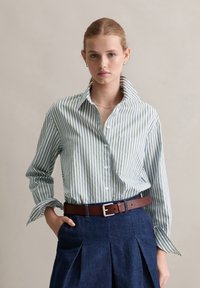 Camicia a righe verde chiaro e bianca, stile button-down con colletto a punta. Abbinata a una gonna in denim scuro e una cintura in pelle marrone.