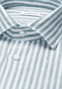 Gros plan d’un col de chemise à rayures verticales vertes et blanches avec des boutons blancs et une étiquette de la marque Seidensticker.