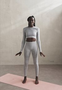 Gray long-sleeve crop top and high-waisted leggings set, made of stretchy material with a subtle pattern, worn by a person on a pink yoga mat.