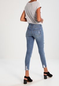 Jeans ajustados de mezclilla azul con dobladillo deshilachado y detalles desgastados, combinados con una camiseta gris y sandalias de tacón cuadrado negras.