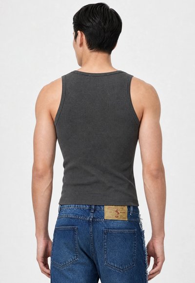 Homme portant un débardeur côtelé sans manches gris foncé et un jean en denim bleu avec un patch en cuir sur la ceinture arrière, vu de dos.