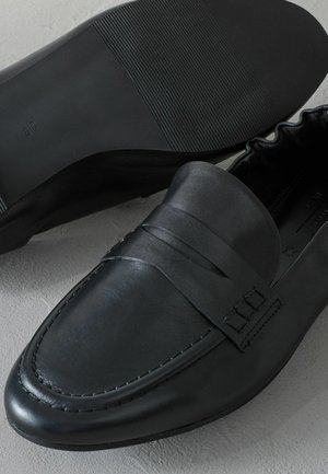 Černé kožené slip-on boty s hladkou texturou, výrazným prošíváním a flexibilní gumovou podrážkou s horizontálními drážkami.