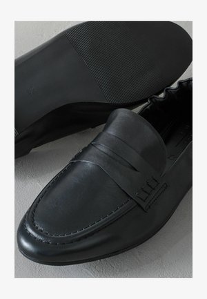 Fekete bőrcipő, amely sima textúrával, jól definiált varrással és rugalmas, vízszintes bordázattal ellátott gumitalppal rendelkezik.