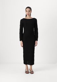 Vestido preto de mangas longas com padrão texturizado geométrico, silhueta ajustada, decote barco e comprimento até a metade da panturrilha, combinado com sandálias pretas de tiras.