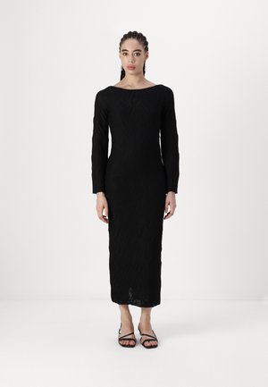 Black long-sleeve dress with geometric textured pattern, fitted silhouette, boat neckline, and mid-calf length, paired with black strappy sandals.
